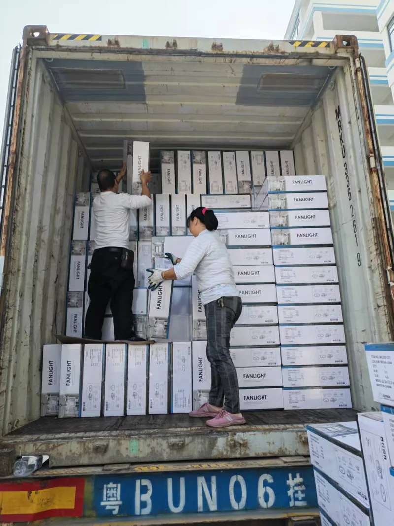Two loaders stacking printed cartons into a wall inside the container